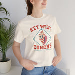 Key West Conchs Premium Lightweight T-Shirt in natural with the grinning striped conch shell mascot inside a teal diamond outline on the front, worn by model