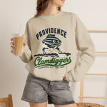 Providence Clamdiggers Crewneck Sweatshirt in sand with the Providence Clamdiggers logo, a quahog clam character in a green cap raking a Narragansett Bay mudflat, with Clamdiggers in green script on the front, worn by model