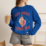 Key West Conchs Crewneck Sweatshirt in royal with the grinning striped conch shell mascot inside a teal diamond outline on the front, worn by model
