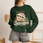 Seattle Clamdiggers Crewneck Sweatshirt in forest green with the Seattle Clamdiggers logo, a clam shell made from a baseball half-buried in a tide flat on the front, worn by model