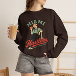 Miami Hustlers Crewneck Sweatshirt in dark chocolate with the mustached man in a striped vest holding playing cards and a bat on the front, worn by model