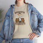 Augusta Tourists Heavyweight T-Shirt in sand with the cartoon ballplayer with a bat standing on a travel trunk on the front, worn by model