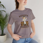 Augusta Tourists Premium Lightweight T-Shirt in pebble brown with the cartoon ballplayer with a bat standing on a travel trunk on the front, worn by model