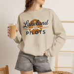 Lakeland Pilots Crewneck Sweatshirt in sand with the airplane propeller nose art over bold navy block lettering on the front, worn by model
