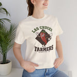 Las Cruces Farmers Premium Lightweight T-Shirt in natural with the Las Cruces Farmers logo, a red chile pepper pitcher in a high-kick windup on a brown diamond, with Farmers in brown block letters on the front, worn by model