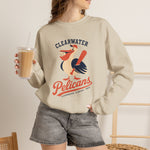 Clearwater Pelicans Crewneck Sweatshirt in sand with the laughing pelican in a red cap swinging a bat with a ball in its beak on the front, worn by model