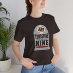 Tombstone Nine Premium Lightweight T-Shirt in brown with the Tombstone Nine logo, a grey headstone topped by a baseball marked 1890, with Base Ball Club and a Territorial Champions banner on the front, worn by model