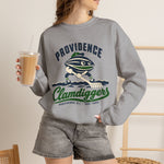 Providence Clamdiggers Crewneck Sweatshirt in sport grey with the Providence Clamdiggers logo, a quahog clam character in a green cap raking a Narragansett Bay mudflat, with Clamdiggers in green script on the front, worn by model