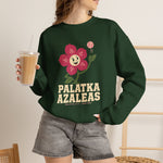 Palatka Azaleas Crewneck Sweatshirt in forest green with the smiling pink flower mascot with two baseballs above it on the front, worn by model